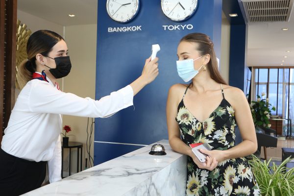 A tourist woman and receptionist at counter in hotel wearing medical masks as precaution against virus. Young woman on a business trip doing check-in at the hotel